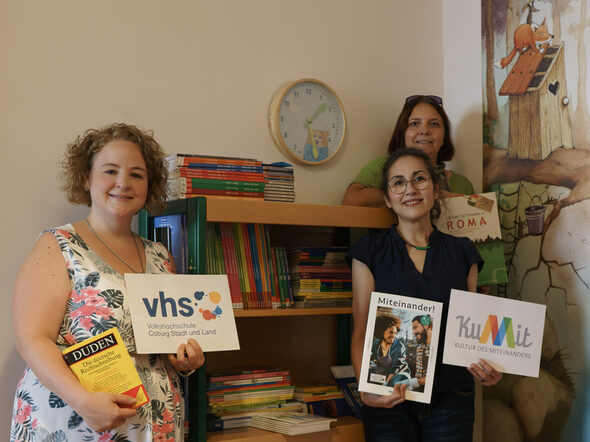 Laura Göldner und Helgard van Sein von der VHS Coburg vor dem neuen Bücherregal im Familienstützpunkt mit Leiterin Katja Fuß.