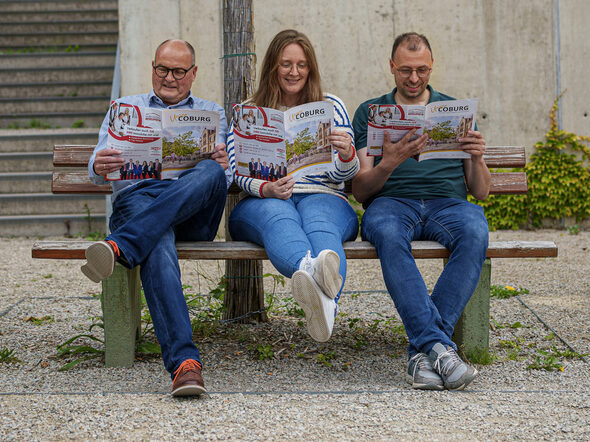 Drei Personen lesen Unser Coburg auf einer Parkbank