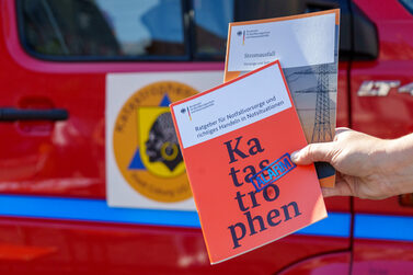 Infobroschüre des Bundesamts für Bevölkerungsschutz und Katastrophenschutz vor einem Einsatzfahrzeug
