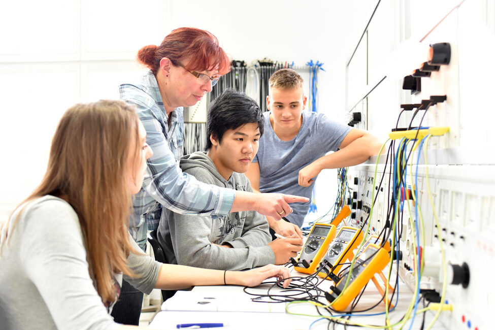 Eine Frau erklärt einer Gruppe Jugendlicher Elektrotechnik