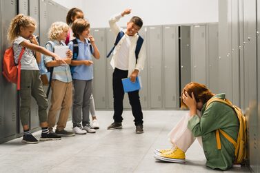 Ein Mädchen ist traurig - andere Schüler zeigen auf das Mädchen