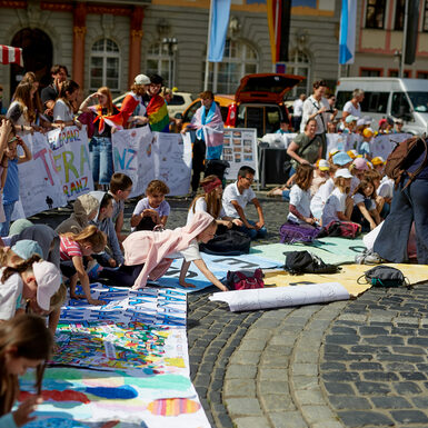 Kinder sitzen auf dem Boden oder stehen rund um selbstgestaltete Plakate zum Thema Toleranz