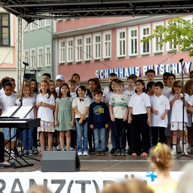 Eine Gruppe von Kindern steht auf der Bühne und singt ein Lied. Sie werden von einer Frau am Keyboard begleitet.