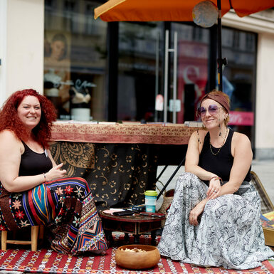 Zwei Frauen sitzen auf Hockern zusammen und lächeln.