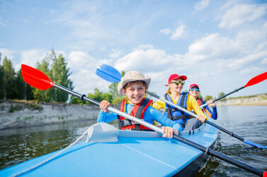 Drei Kinder und Jugendliche fahren mit dem Kajak auf einem Fluss.