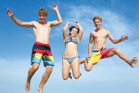 Drei Jugendliche in Badekleidung springen von einem Steg ins Wasser