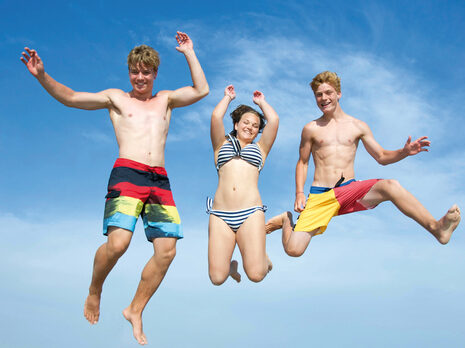 Drei Jugendliche in Badekleidung springen von einem Steg ins Wasser