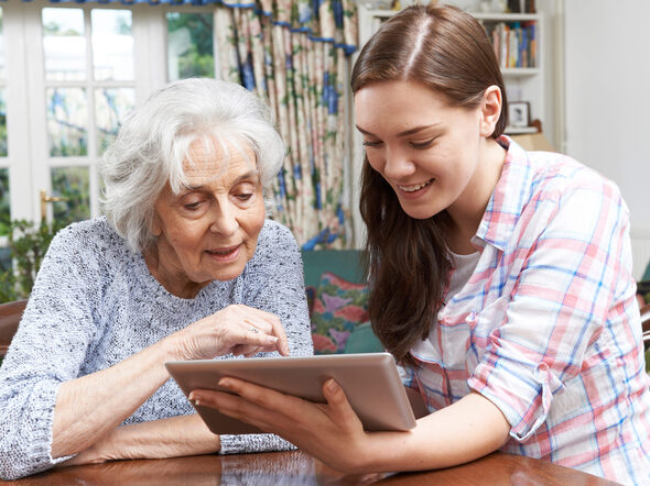 Jugendliche erklärt älterer Frau die Bedienung eines Tablet-Computers